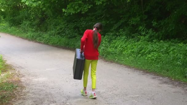 Fille, marche dans les bois avec une lourde valise noire. 4k, tir au ralenti, tir au steadicam . — Video