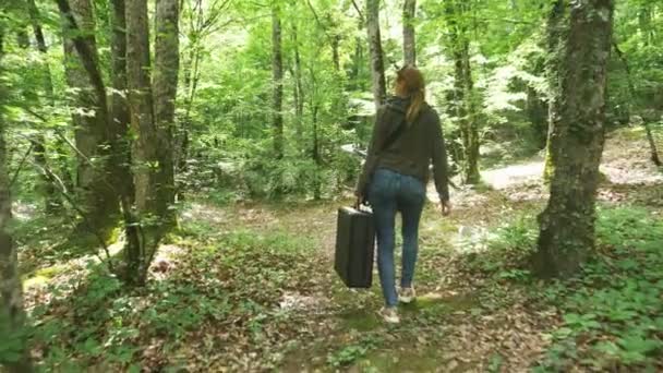 Ragazza, cammina nel bosco con una pesante valigia nera. 4k, tiro al rallentatore, tiro stazionario . — Video Stock