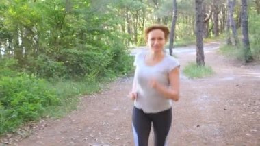 Uzak bir iz güneşli yaz ormanda çalışan kadın. spor etkinliği açık havada, eğitim ve güzel doğa egzersiz motivasyon. Güneş parlamayı, yavaş hareket 4k, steadicam vurdu