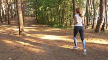 Uzak bir iz güneşli yaz ormanda çalışan kadın. spor etkinliği açık havada, eğitim ve güzel doğa egzersiz motivasyon. Güneş parlamayı, yavaş hareket 4k, steadicam vurdu