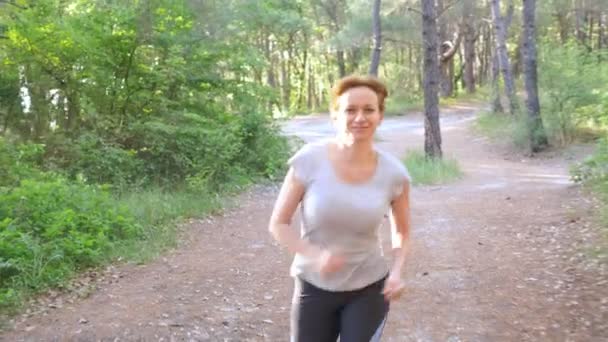 Femme s'enfuyant sur un sentier dans la forêt ensoleillée d'été. motivation pour l'activité sportive en plein air, l'entraînement et l'exercice dans une belle nature. éblouissement solaire, ralenti 4k, coup de steadicam — Video