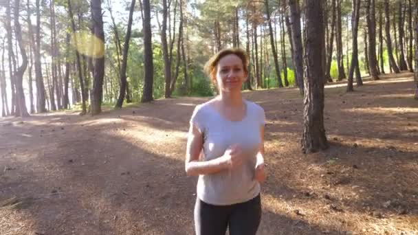 Mujer huyendo por un sendero en el soleado bosque de verano. motivación para la actividad deportiva al aire libre, entrenamiento y ejercicio en la hermosa naturaleza. deslumbramiento solar, cámara lenta 4k, disparo steadicam — Vídeos de Stock