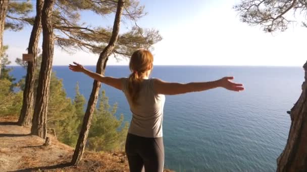Жінка фітнес бігун на вершині щасливий і святкує успіх. жінка насолоджується видом на море з гори, вона піднімає руки і відчуває свободу і дихання вітру. 4k, повільний рух — стокове відео