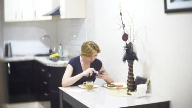 kadın mutfakta evde pizza yiyor ve onun smartphone, 4 k, kullanarak arka plan bulanıklık