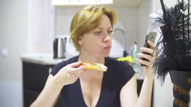 kadın mutfakta evde pizza yiyor ve onun smartphone, 4 k, kullanarak arka plan bulanıklık
