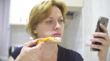 kadın mutfakta evde pizza yiyor ve onun smartphone, 4 k, kullanarak arka plan bulanıklık