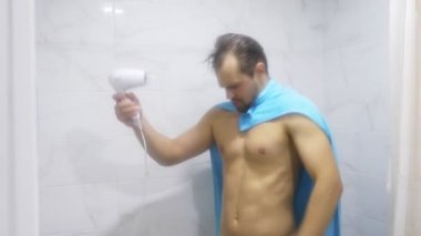 Genç yakışıklı kaslı adam banyoda duş sonra. O bir Süpermen tasvir ve kendini bir fön üfleme onun omuzlarında bir havlu ver. 4k
