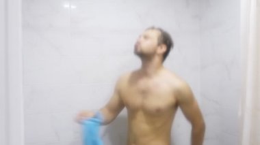 Genç yakışıklı kaslı adam bir duş alır. adam şarkı söylüyor ve bir havlu ile duşta dans ediyor. 4k