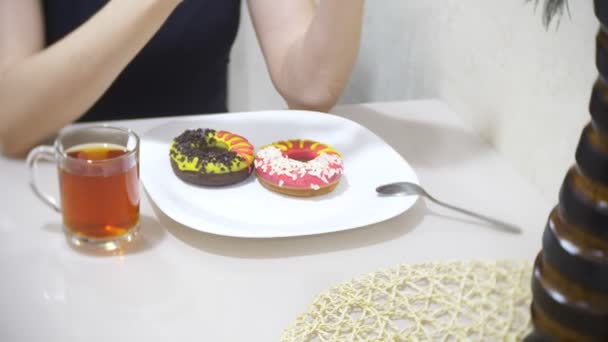 Mujer comiendo rosquillas dulces con esmalte de color en la cocina en casa y utilizando su teléfono inteligente, 4k, fondo borroso — Vídeos de Stock