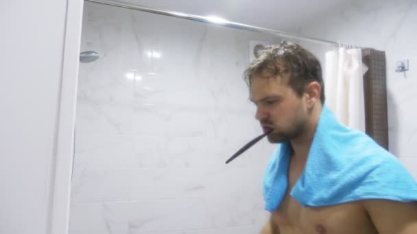 Giovane uomo muscoloso bello dopo la doccia in bagno. Si mise un asciugamano sulle spalle, ritraendo il superuomo e lavandosi i denti allo specchio. 4k — Video Stock