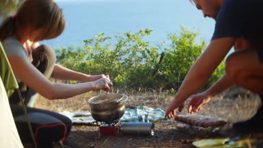 bir erkek ve bir kadın, kampçılar, aşçılar yemek yanında deniz manzara muhteşem manzaralı pine Grove dik bir sahil kenarında bir çadır. 4k