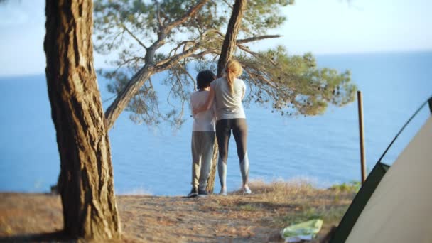 Une mère de famille heureuse et son fils et sa fille vont au bord d'une côte escarpée avec une pinède. ils bénéficient d'une vue magnifique sur le paysage marin. 4k . — Video