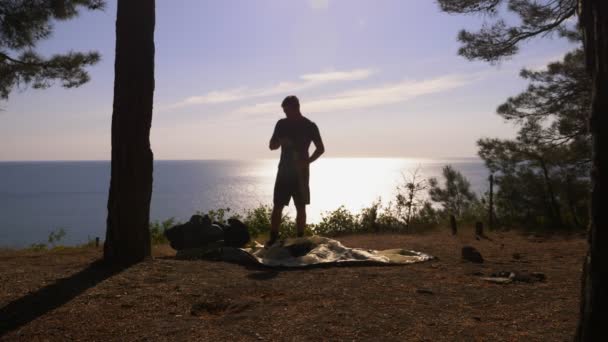 실루엣 관광 남자는 큰 배낭에 소나무 숲과 가파른 깎아지른 듯한 바다 해안의 가장자리에 여행. 함께 바다 풍경의 아름 다운 볼 수 있습니다. 4 공화국 슬로우 모션 — 비디오