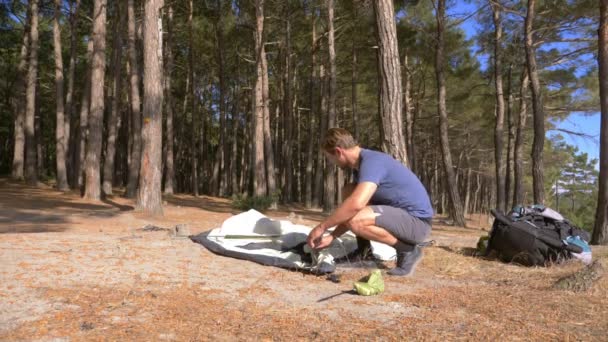 A male tourist arranges a tent on the edge of a steep coastal shore in a pine grove with a magnificent view of the seascape. 4k. — Stock Video