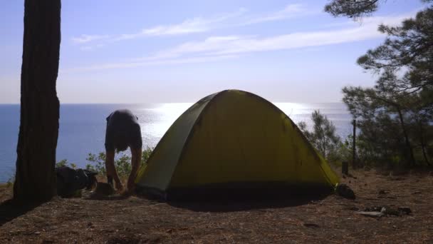 一位男性游客在一座松树林陡峭的海滨海岸的边缘上布置了一座帐篷, 海景的壮丽景色。4k. — 图库视频影像