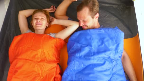 Primer plano. Una linda pareja abrazándose dentro de una tienda de campaña acostada en sacos de dormir, coquetean y se besan, 4k . — Vídeos de Stock
