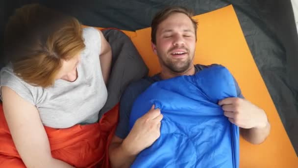 Primer plano. Una linda pareja abrazándose dentro de una tienda de campaña acostada en sacos de dormir, coquetean y se besan, 4k . — Vídeos de Stock