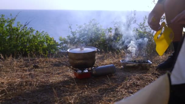 Muž na šířku táborníci, kuchaři jídlo vedle stanu na okraji strmého pobřeží v borovém háji s nádherným výhledem na moře. 4k — Stock video