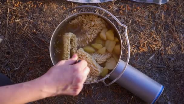 Een vrouw, de kampeerders, kookt eten naast een tent aan de rand van een steile kustlijn in een pijnbomenbos met een prachtig uitzicht op het landschap van de zee. 4k — Stockvideo