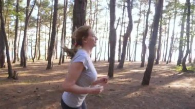 Uzak bir iz güneşli yaz ormanda çalışan kadın. spor etkinliği açık havada, eğitim ve güzel doğa egzersiz motivasyon. Güneş parlamayı, yavaş hareket 4k, steadicam vurdu