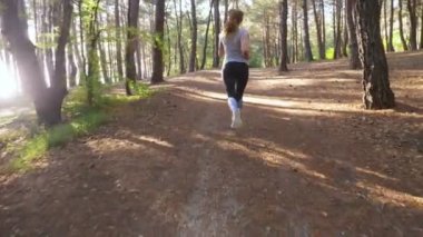 Uzak bir iz güneşli yaz ormanda çalışan kadın. spor etkinliği açık havada, eğitim ve güzel doğa egzersiz motivasyon. Güneş parlamayı, yavaş hareket 4k, steadicam vurdu