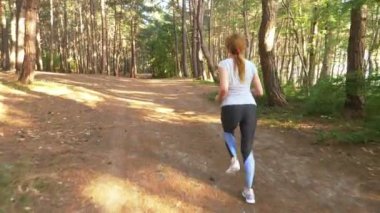 Uzak bir iz güneşli yaz ormanda çalışan kadın. spor etkinliği açık havada, eğitim ve güzel doğa egzersiz motivasyon. Güneş parlamayı, yavaş hareket 4k, steadicam vurdu