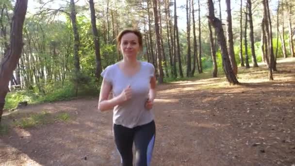 Mujer huyendo por un sendero en el soleado bosque de verano. motivación para la actividad deportiva al aire libre, entrenamiento y ejercicio en la hermosa naturaleza. deslumbramiento solar, cámara lenta 4k, disparo steadicam — Vídeos de Stock