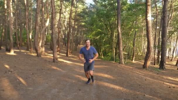 Hombre huyendo en un sendero en el soleado bosque de verano. motivación para la actividad deportiva al aire libre, entrenamiento y ejercicio en la hermosa naturaleza. deslumbramiento solar, cámara lenta 4k, disparo steadicam — Vídeo de stock