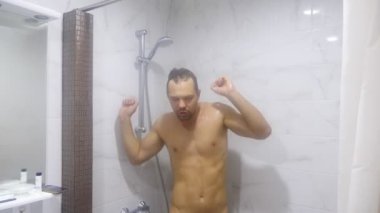 Genç yakışıklı kaslı adam bir duş alır. adam şarkı söylüyor ve duşta dans ediyor. 4k