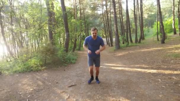 Hombre huyendo en un sendero en el soleado bosque de verano. motivación para la actividad deportiva al aire libre, entrenamiento y ejercicio en la hermosa naturaleza. deslumbramiento solar, cámara lenta 4k, disparo steadicam — Vídeos de Stock