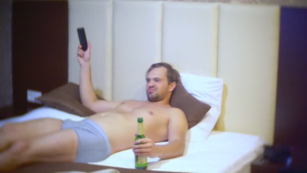 Мужчина смотрит телевизор и пьет пиво дома на кровати. 4k — стоковое видео