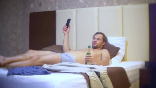 Man tv kijken en het drinken van bier thuis op een bed. 4k — Stockvideo