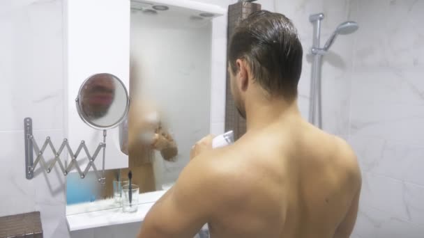 Genç yakışıklı kaslı adam banyoda duş sonra. adam aynaya bakar ve saç kurutma makinesi kurur. 4k — Stok video
