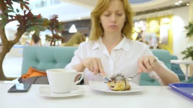 Bir topuz tarçın bir kafeterya ve içecekler kahve rulo bıçak ve çatal ile beyaz bir gömlek bir kadında yiyor. Kahvaltı kavramı. 4k