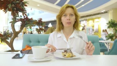 Bir topuz tarçın bir kafeterya ve içecekler kahve rulo bıçak ve çatal ile beyaz bir gömlek bir kadında yiyor. Kahvaltı kavramı. 4k