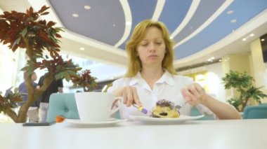 Bir topuz tarçın bir kafeterya ve içecekler kahve rulo bıçak ve çatal ile beyaz bir gömlek bir kadında yiyor. Kahvaltı kavramı. 4k