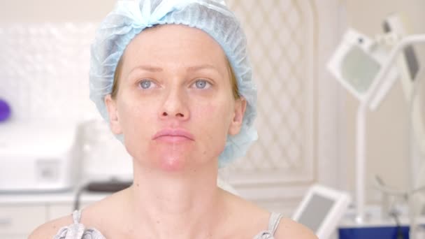 Paciente mujer en un sombrero higiénico espera el procedimiento en el consultorio médico. Primer plano. 4k — Vídeos de Stock