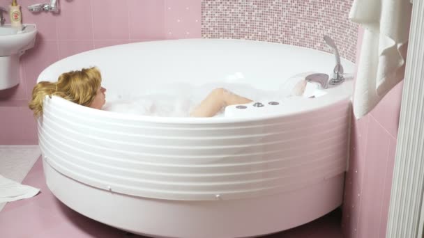 Bella giovane donna si rilassa in un bagno con idromassaggio, su uno sfondo blu. Concetto: procedure termali, massaggi corpo, crema spa, relax, trattamenti acqua. 4k, rallenta. vista dall'alto — Video Stock