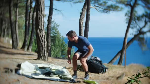 Mužské turistické uspořádá stan na okraji strmé pobřežní pobřeží v borovém háji s nádherným výhledem přímořská krajina. 4k. — Stock video