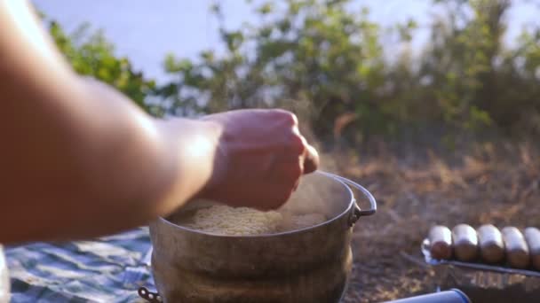 Женщина, отдыхающие, готовит еду рядом с палаткой на краю крутой береговой линии в сосновой роще с великолепным видом на морской пейзаж. на заднем плане, яхта плавает у моря, и — стоковое видео