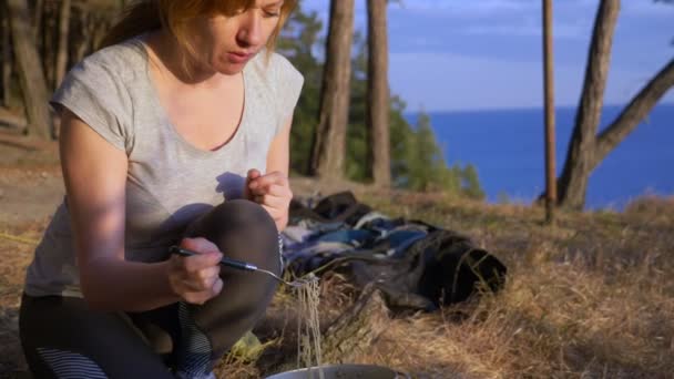 De vrouw, rusten, kookt eten naast de tent aan de rand van een steile kustlijn in een pijnbomenbos met een prachtig uitzicht op het Zeegezicht. 4k. — Stockvideo