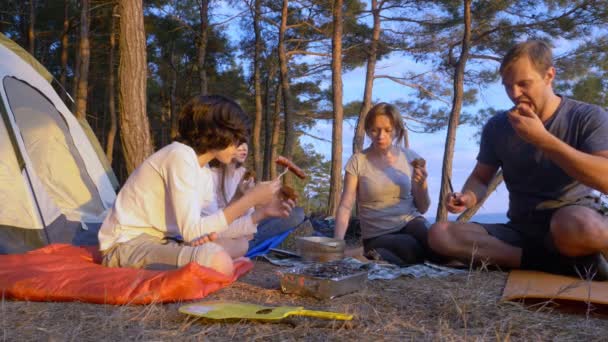 Eine glückliche Touristenfamilie, die neben einem Zelt am Rande einer steilen Küste in einem Pinienhain mit herrlichem Blick auf das Meer Lagerkost isst. 4k. — Stockvideo