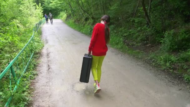 Chica, camina por el bosque con una pesada maleta negra. 4k, disparo en cámara lenta, disparo steadicam . — Vídeos de Stock