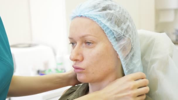 De arts schoonheidsspecialiste zet op een wegwerp hygiënische cap op de vrouwelijke patiënt. concept van schoonheid en cosmetologie. 4 k. contour kunststof — Stockvideo