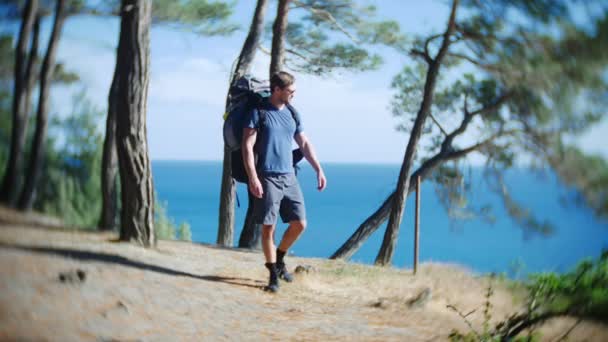 Silhouet toeristische man met een grote rugzak reist naar de rand van een steile steile kust met pijnbomen. met een prachtig uitzicht op het landschap van de zee. 4 k. Slowmotion — Stockvideo