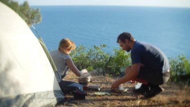 bir erkek ve bir kadın, kampçılar, aşçılar yemek yanında deniz manzara muhteşem manzaralı pine Grove dik bir sahil kenarında bir çadır. 4k