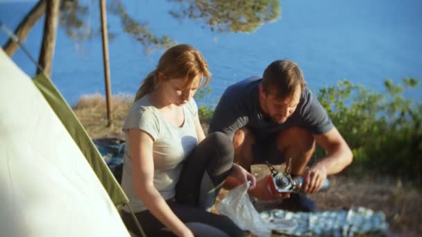 Мужчина и женщина, отдыхающие, готовят еду рядом с палаткой на краю крутой береговой линии в сосновой роще с великолепным видом на морской пейзаж. 4k — стоковое видео