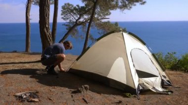 erkek bir turist bir çadır pine Grove dik kıyı kıyı kenarında deniz manzarası muhteşem bir görünüm ile düzenler. 4k.