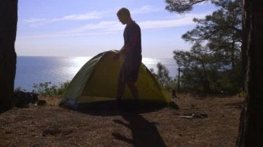 erkek bir turist bir çadır pine Grove dik kıyı kıyı kenarında deniz manzarası muhteşem bir görünüm ile düzenler. 4k.