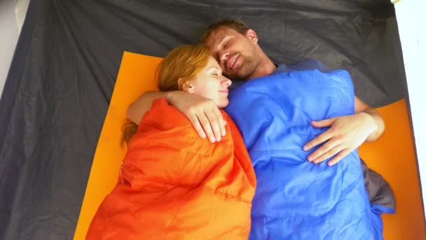 Closeup. A cute couple hugging inside a tent lying in sleeping bags, they flirt and kiss, 4k. — Stock Video